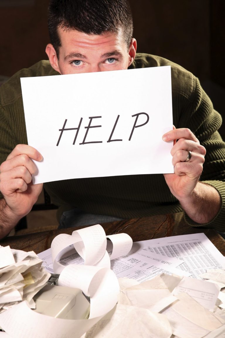 Person holding a sign that says "HELP" amidst scattered bills on a desk.