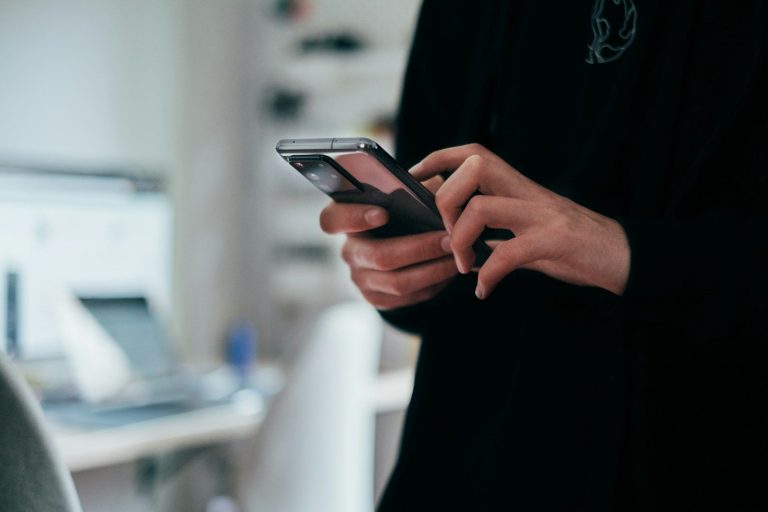 A person using a smartphone while standing in an office or home environment.