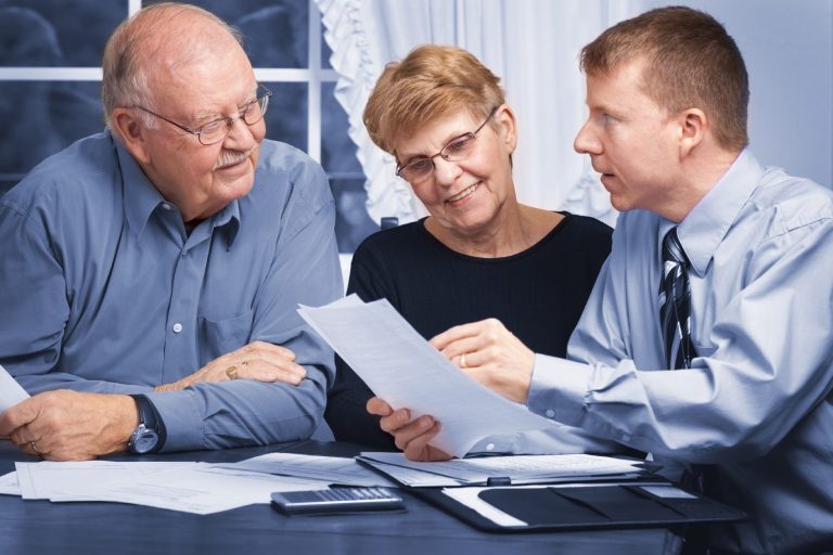 Three people discussing bills at a table, with one person explaining details on how to prevent overpaying and save money.