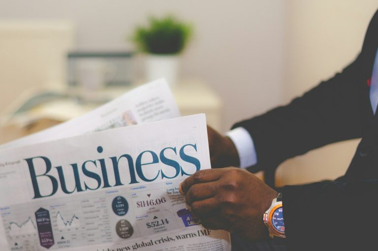 A person holding a business newspaper, with a plant visible in the background.